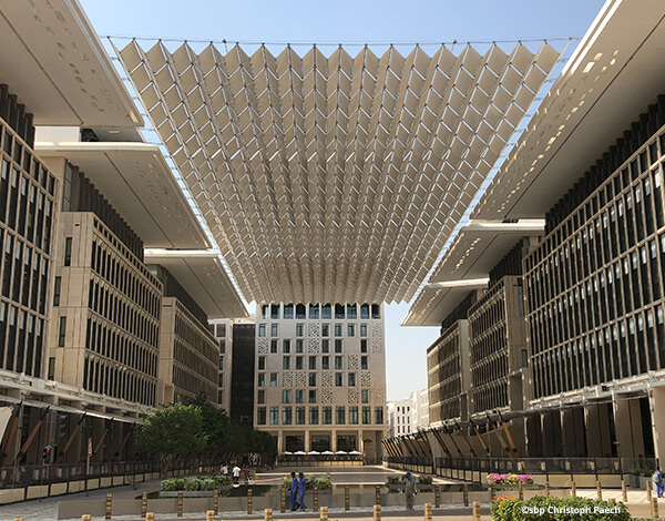Large tensile canopy spanning an open pedestrian plaza between modern buildings.